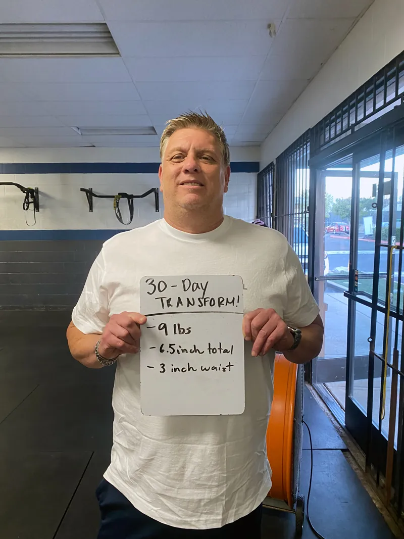 Member holding a 30-day transformation board: minus 9 pounds, 6.5 inches total, 3 inches off waist