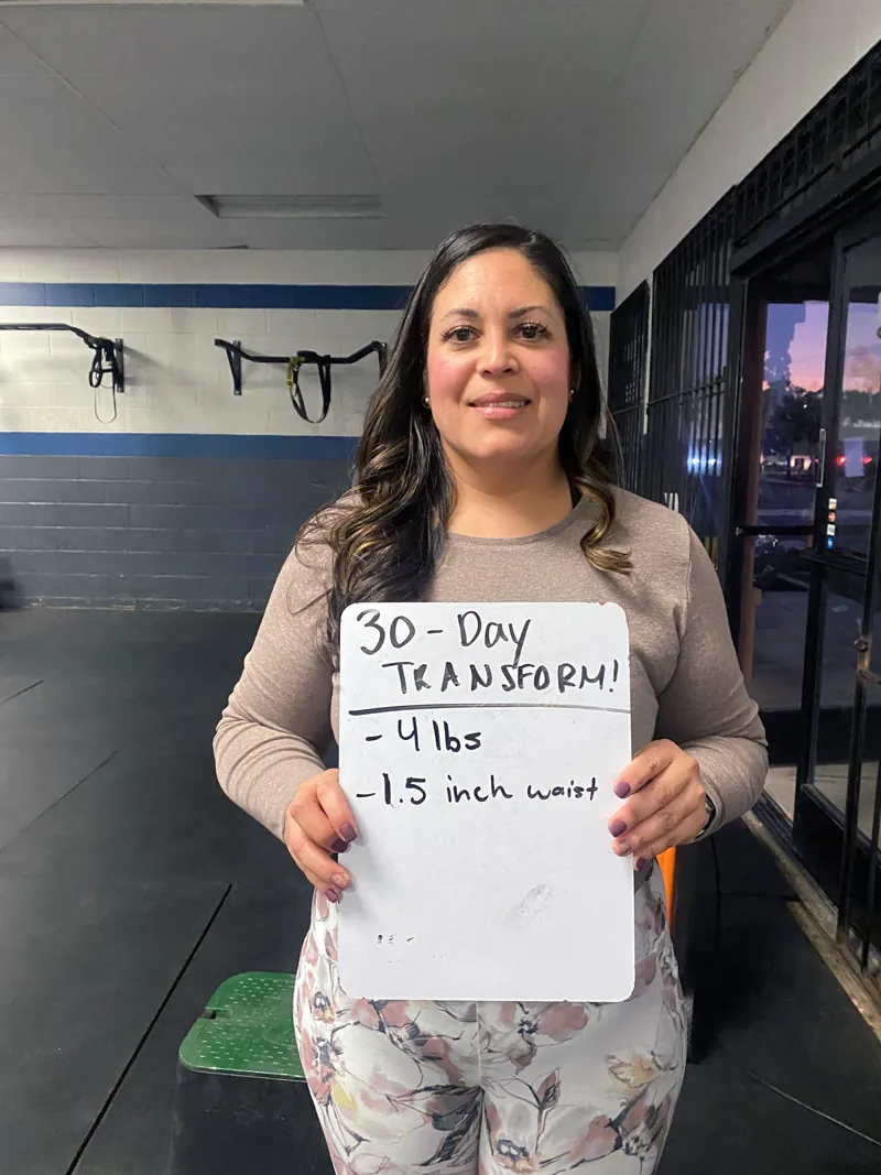 Member holding a 30-day transformation board: minus 4 pounds, 1.5 inches off waist